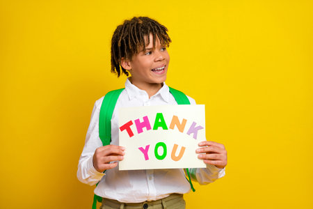 Happy schoolboy expressing gratitude and joy holding a colorful thank you sign on a yellow backgroundの写真素材