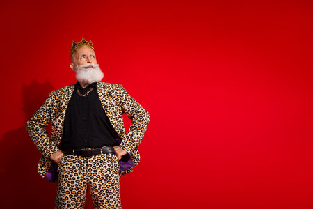 Stylish elderly man posing confidently in a leopard print suit against a vibrant red backdropの写真素材