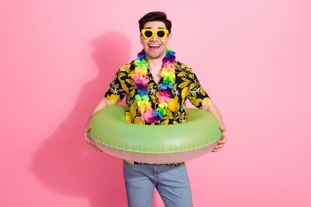 Smiling young man in tropical outfit with inflatable ring and summer accessories enjoying leisure...