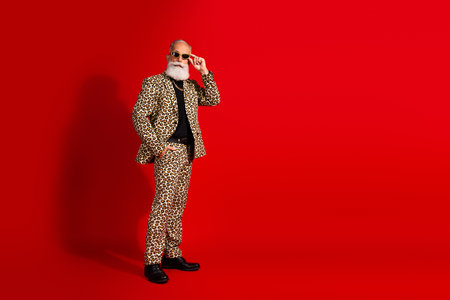 Fashion model elderly man in leopard print suit posing confidently against a bold red background exuding eleganceの写真素材