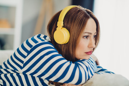 Young Woman Relaxing at Home Wearing Yellow Headphones and a Striped Sweatshirt, Enjoying the Comfort of a Warm and Casual Day Indoorsの写真素材