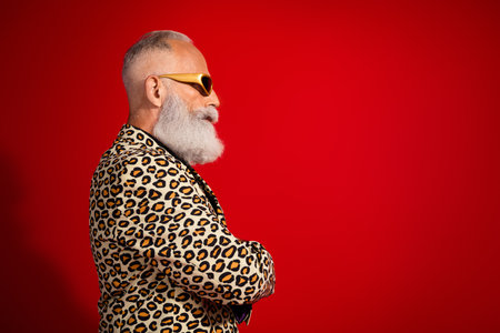 Stylish and charismatic elderly man wearing a leopard print jacket and sunglass against a vibrant red backgroundの写真素材