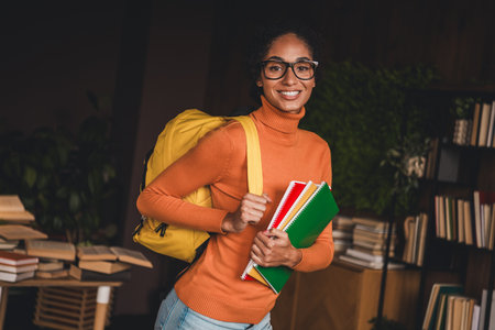 Young woman in turtleneck sweater smiles brightly while holding colorful notebooks, embodying the...