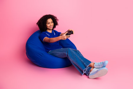 Young woman enjoying leisure time sitting on a bean bag while holding a controller against a vibrant...