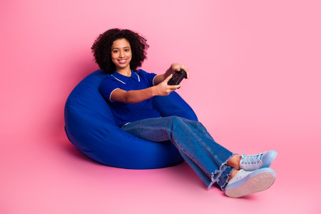 Smiling young woman relaxing on a bean bag chair with a gaming controller on a vibrant pink...