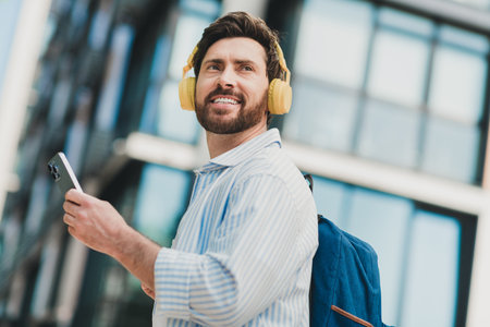 Young man enjoying music on headphones while holding a smartphone outdoors on a bright sunny day in the cityの写真素材