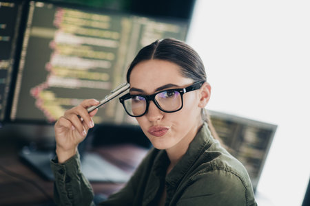 Young female programmer analyzing code at her workspace with monitors in a modern and professional...