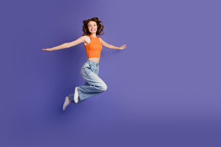 Cheerful girl in casual fashion a stylish young girl posed jumping with energy against a purple...