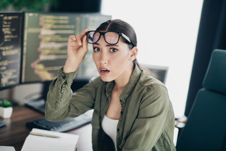 Young female programmer surprised while coding on a computer in a modern office setting, showcasing...