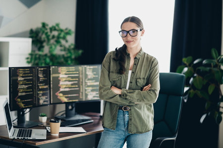 Confident female programmer standing in stylish office workspace while coding on multiple computer...