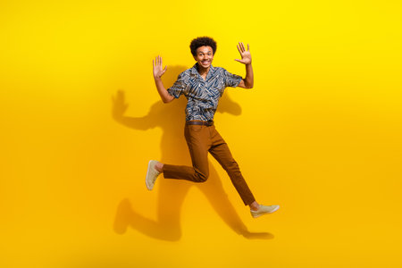 Happy young man jumping with raised hands against a vibrant yellow background, expressing excitement