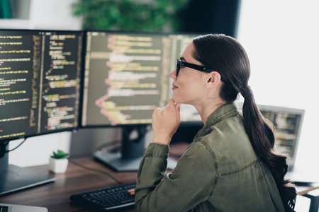 Professional computer programmer analyzing code on multiple monitors in a modern office workspace settingの写真素材