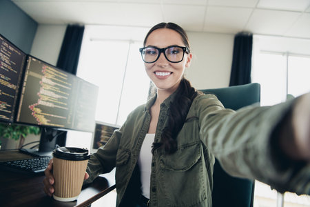 Young female programmer enjoys a refreshing coffee while working remotely in a modern workspace with multiple computer monitorsの写真素材