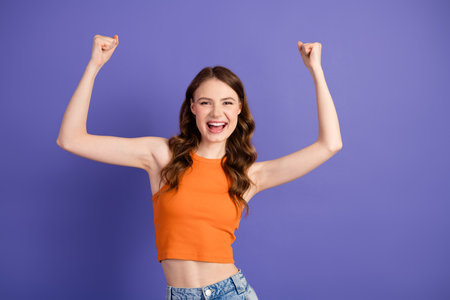 Cheerful and confident with raised arms, expressing joy in casual attire against a vibrant purple backgroundの写真素材