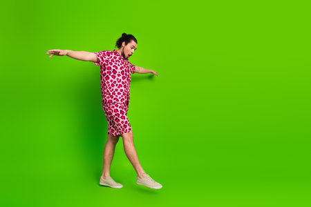 Vibrant young man in pink leopard print outfit posing against a striking green background showcasing fashion vibrancyの写真素材