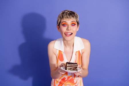 Young woman with vibrant style enjoying a chocolate dessert against a vivid purple background with joyful expressionの写真素材