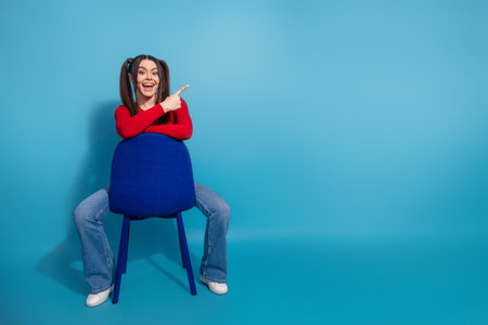 Cheerful Young Girl Posing Playfully on Blue Background in Stylish Red Shirt and Jeansの写真素材