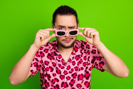 Young man wearing pink leopard print shirt and sunglass posing against green backdrop with a confident expressionの写真素材