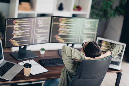 Young professional woman enjoying a break at her workspace with coding on monitors in a casual...