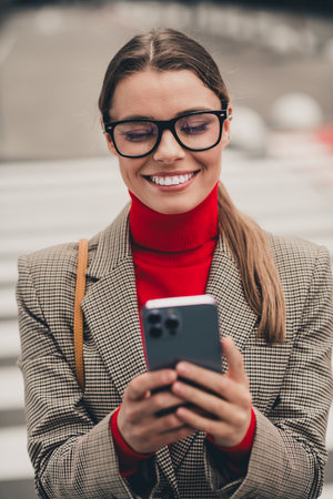 Confident businesswoman in formal attire using smartphone outside in urban environment with a professional demeanorの写真素材