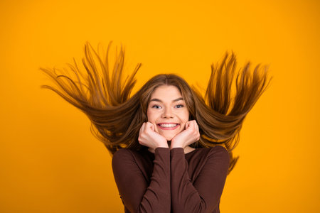 Stylish young woman with flowing hair smiling joyfully against vibrant yellow backdrop showcasing happiness and energyの写真素材