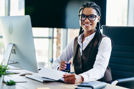 Confident professional businesswoman at an office desk, working on a computer, showcasing leadership and modern corporate styleの写真素材