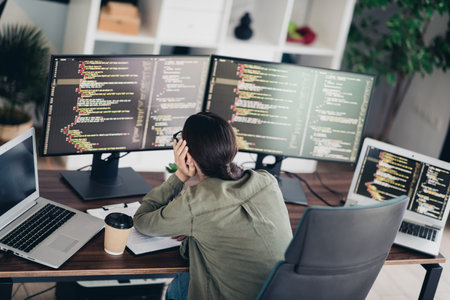 Young female programmer working at a desk with multiple computers coding software in a modern home officeの写真素材