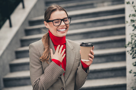 Young professional businesswoman enjoying coffee while outdoors in elegant attire, with a confident and charming smileの写真素材