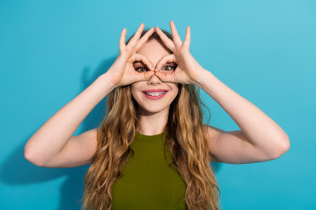 Playful girl with braces making a fun gesture against a vivid blue background, wearing green attire and exuding cheerful energyの写真素材