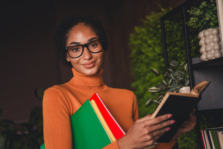 Young woman studying at home, holding colorful books while reading in a cozy apartment