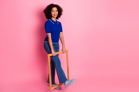 Stylish young female posing playfully with a wooden frame against vibrant pink background in trendy...