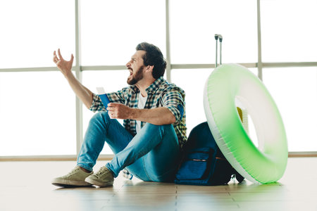 Excited traveler holding his ticket in an airport terminal, ready for his holiday adventure, sitting among travel propsの写真素材