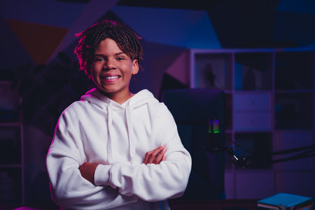 Confident teen in hoodie with microphone setup in neon lit room, portraying gamer and aspiring content creatorの写真素材