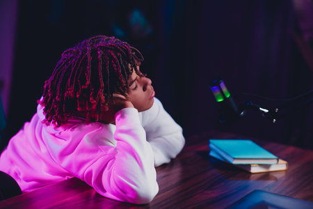 Young man with dreadlocks in vibrant lighting recording a podcast from home wearing a white hoodieの写真素材