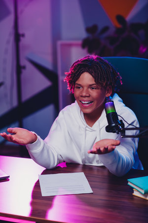 Teen capturing the moment as a host with microphone at desk in a neon-lit roomの写真素材
