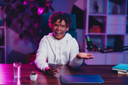 Young male gamer and vlogger in stylish setting creating online streaming content with a microphone and computerの写真素材