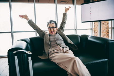 Confident businesswoman celebrating success in a stylish modern office setting with natural lighting and a city viewの写真素材