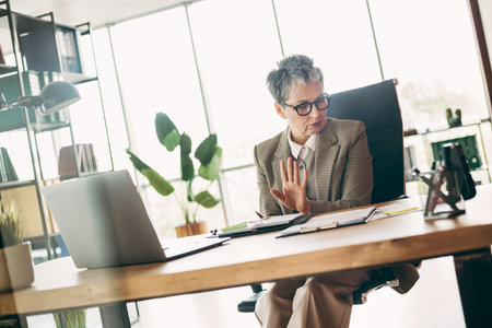 Confident Businesswoman Sitting in Office Environment Focused on Work with Documents and Laptops Emphasizing Professional Successの写真素材