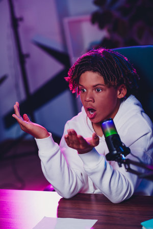 Teen content creator recording a podcast in vibrant neon lighting with a microphone, showcasing expression and modern online trendsの写真素材