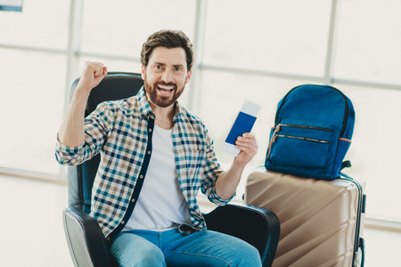 Excited man celebrating at airport departure area with passport, ready for international summer travel and adventureの写真素材