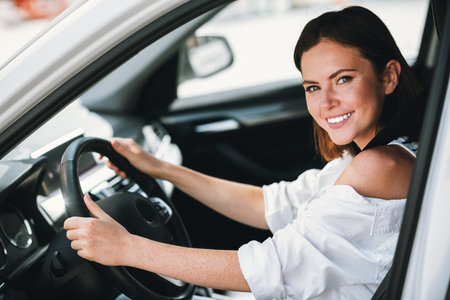 Smiling young woman driving car in daylight, enjoying her ride through the city streets