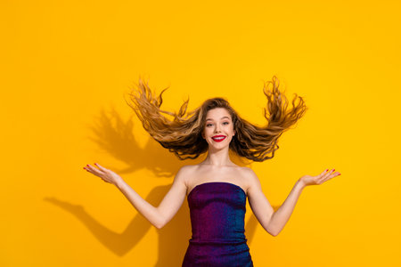 Vibrant young woman in stylish dress flipping her hair against a bright yellow background exuding confidence and joyの写真素材