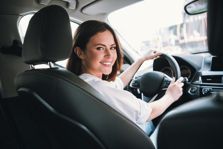 Young woman smiling while driving a car on a sunny day, enjoying a weekend getawayの写真素材