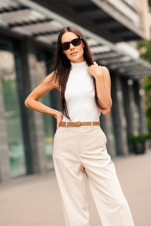 Stunning brunette woman poses confidently outdoors in urban setting wearing chic summer outfit with sunglassesの写真素材