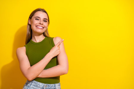 Smiling Young Woman in Stylish Khaki Top Points Cheerfully Against Bright Yellow Background Suggesting Ideas or Promoting Conceptsの写真素材