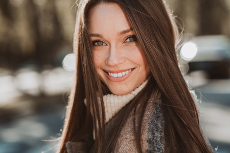 Glamorous woman with long brunette hair smiling outdoors in sunny autumn parkの写真素材