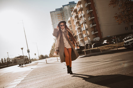 Beautiful woman walking in the city on a sunny autumn day enjoying urban life and fall fashion styleの写真素材