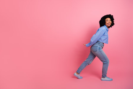 Charming young woman in a stylish casual attire posing on a pink background with a cheerful and confident atmosphereの写真素材