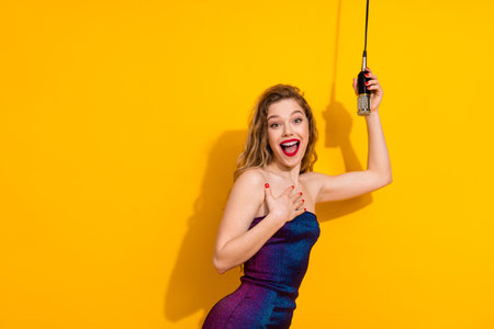 Excited young woman holding a microphone with a cheerful expression against a vibrant yellow backgroundの写真素材