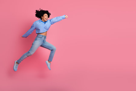 Joyful young woman jumping dynamically against a pink background, expressing energy, happiness, and a carefree lifestyleの写真素材